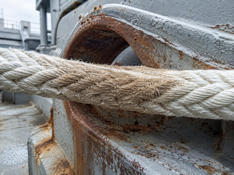Close-up of a synthetic mooring rope where it bears against the lip of a steel fairlead, showing surface wear concentrated in a narrow band